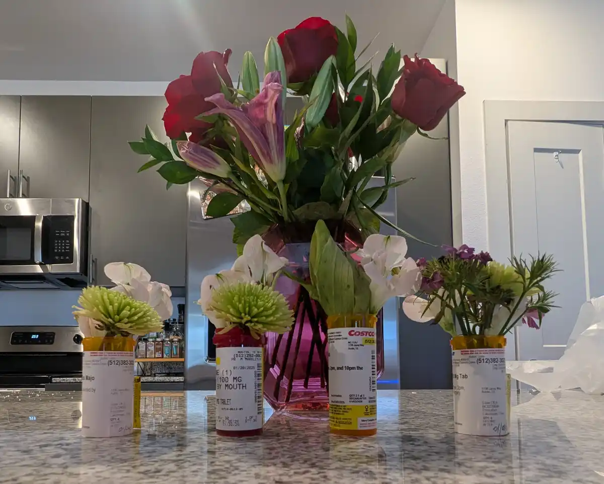 A kitchen counter displays several bouquets of fresh flowers, including red roses and white lilies, arranged in repurposed…