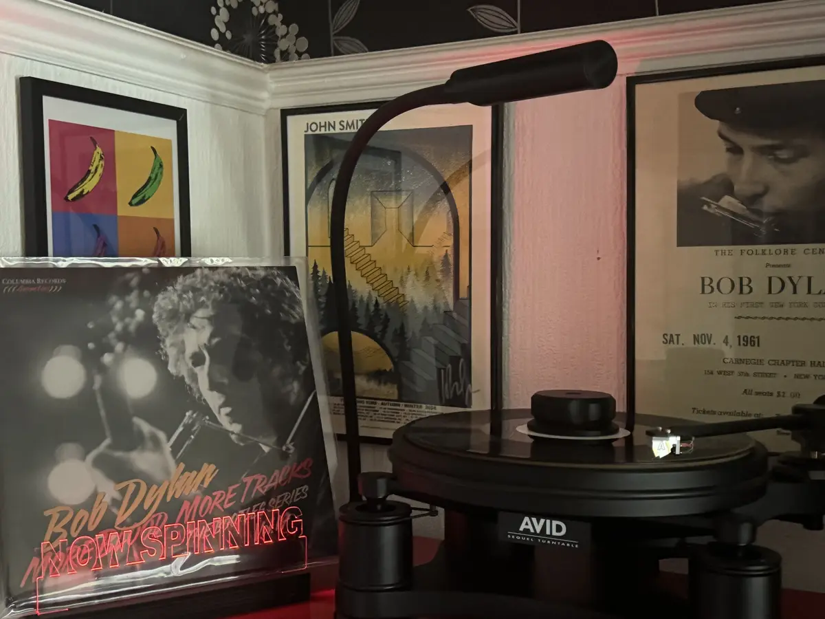 A black turntable sits on a red surface with a Bob Dylan album cover leaning against it, overlaid with glowing red text…