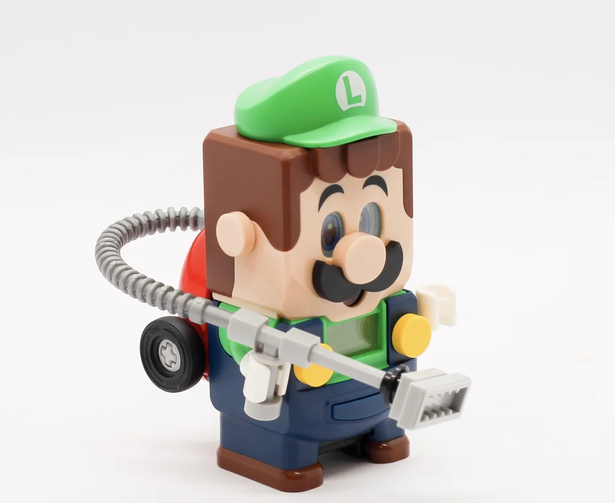 A Lego-style figurine of Luigi, recognizable by his green cap with an 'L' and blue overalls, is depicted holding a gray…