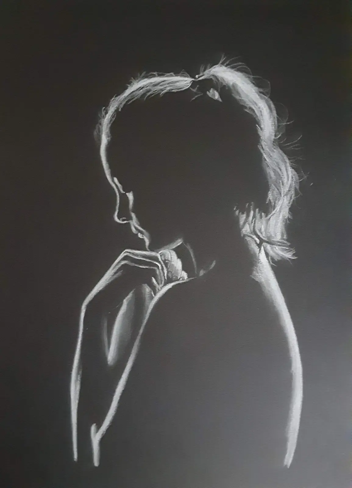 A chalk drawing on a dark surface shows a person in profile with their hand near their face, hair tied back, and the face is…