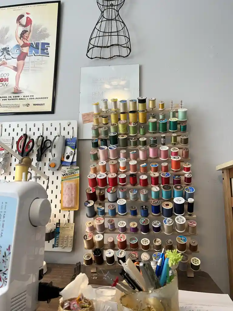 A well-organized sewing station features a large wooden rack filled with hundreds of spools of thread in every color…