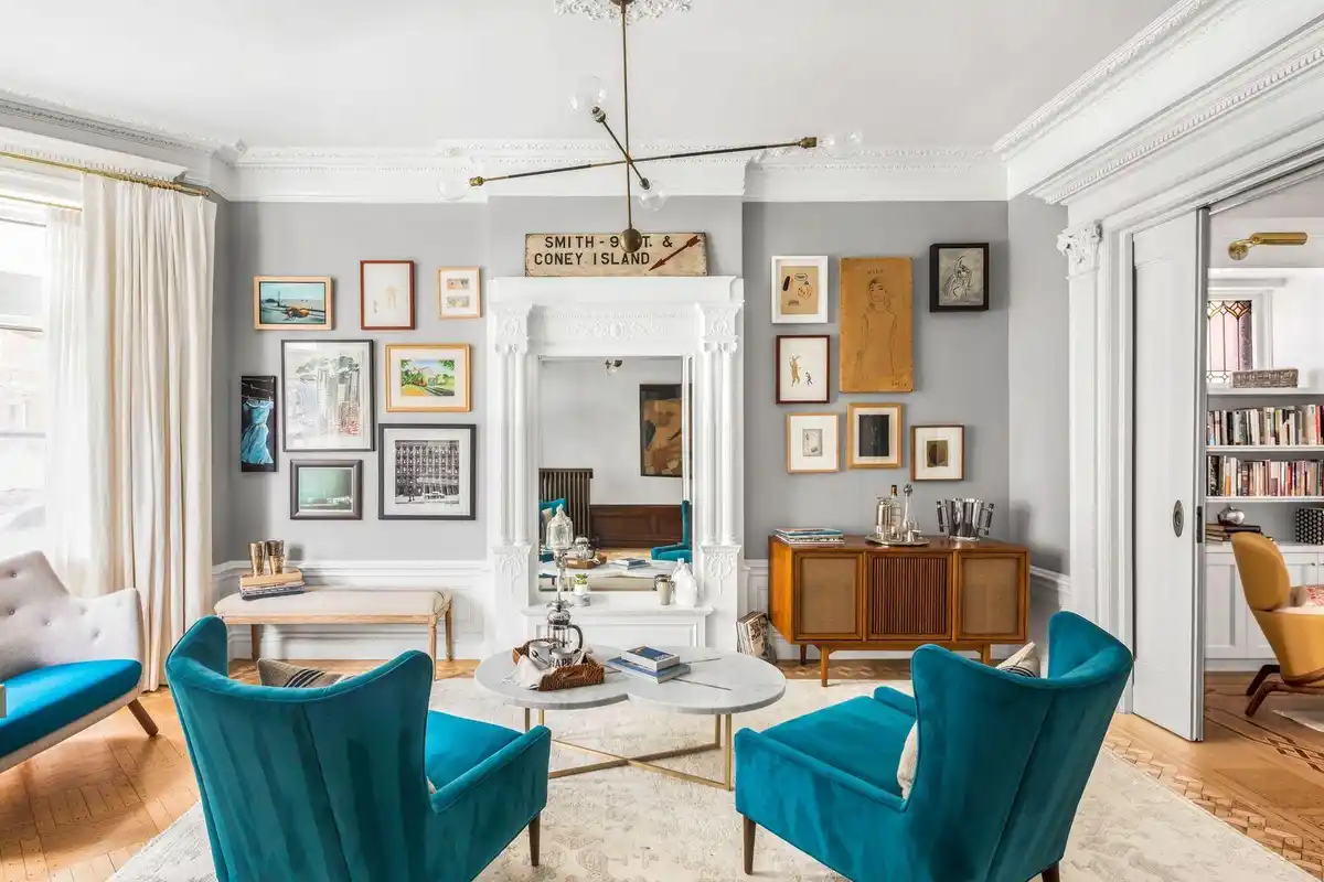 A stylishly decorated living room with gray walls, white trim, and two bright teal velvet armchairs facing each other across…