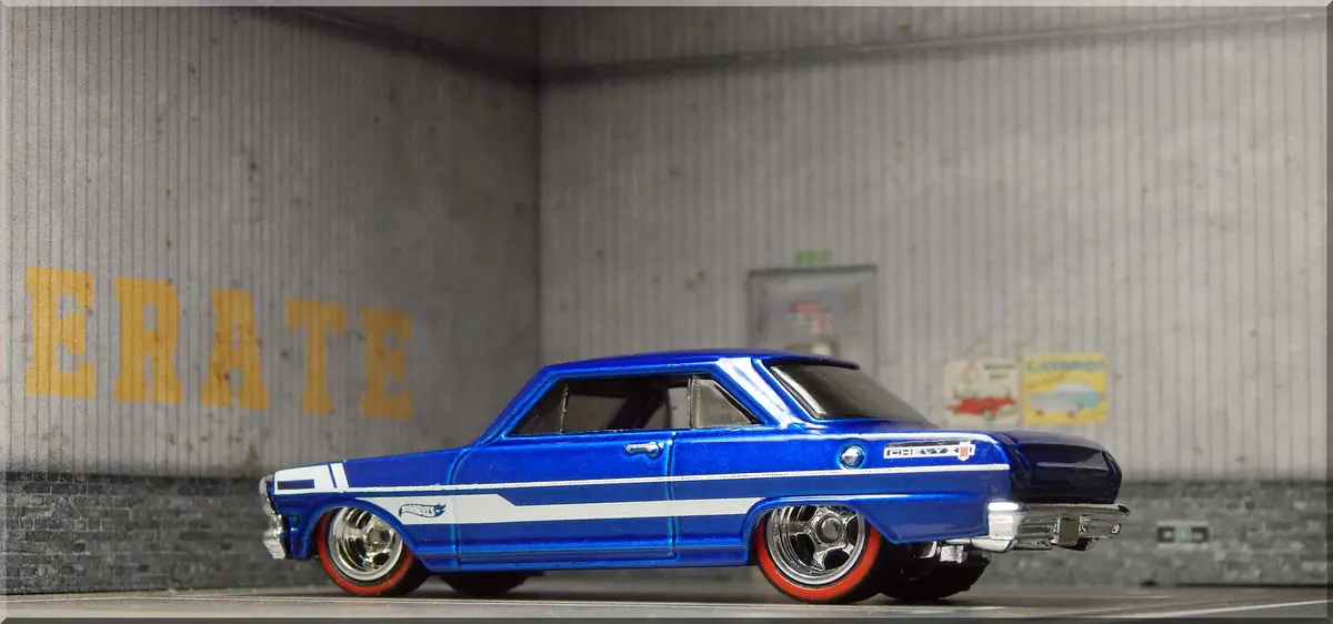 A blue Hot Wheels die-cast model of a classic Chevrolet car is shown in profile, parked in front of a corrugated metal wall…