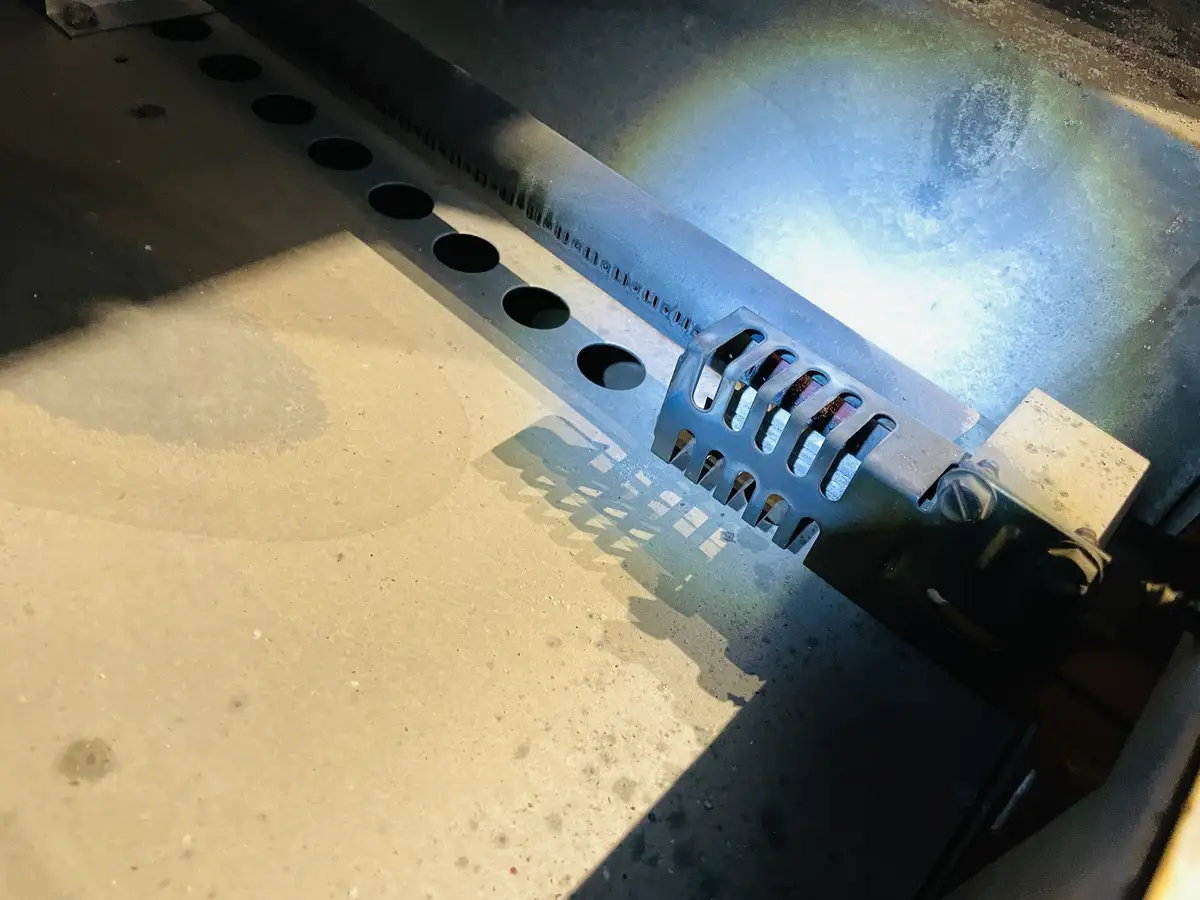 A close-up photo shows a metal printer component, likely a print head or carriage, with a row of circular holes and a…