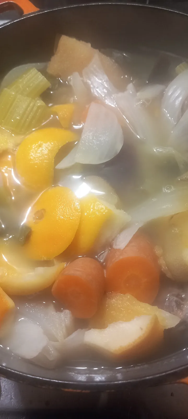 A close-up photo shows a pot of boiling water with various chopped vegetables including carrots, onions, celery, and yellow…