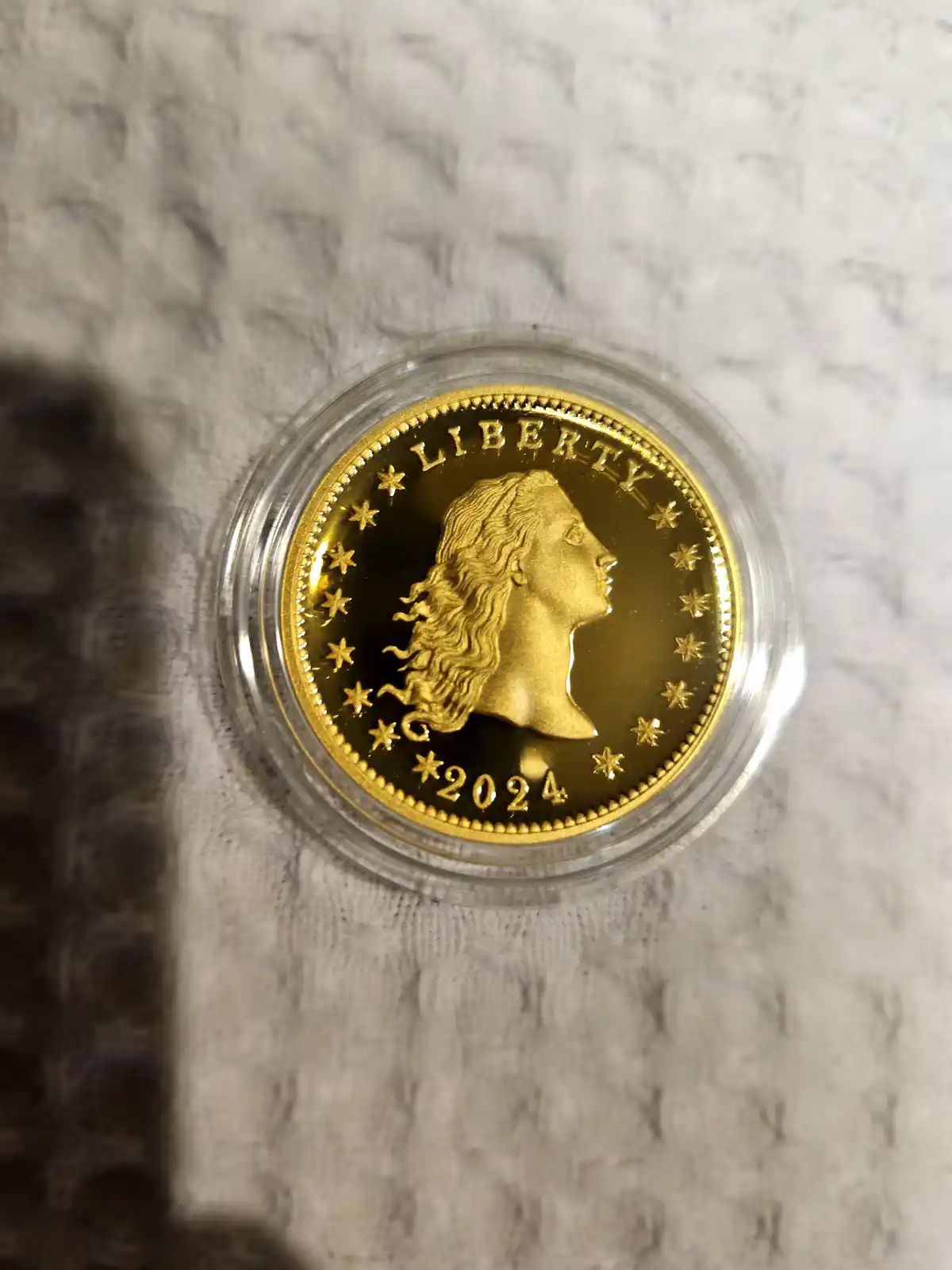 A close-up photo shows a gold-colored coin with a profile of Lady Liberty, surrounded by stars and the word 'LIBERTY' along…