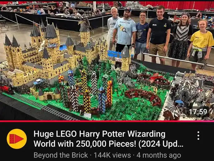 A group of six people stands behind a massive, intricate LEGO model of the Harry Potter wizarding world, featuring Hogwarts…