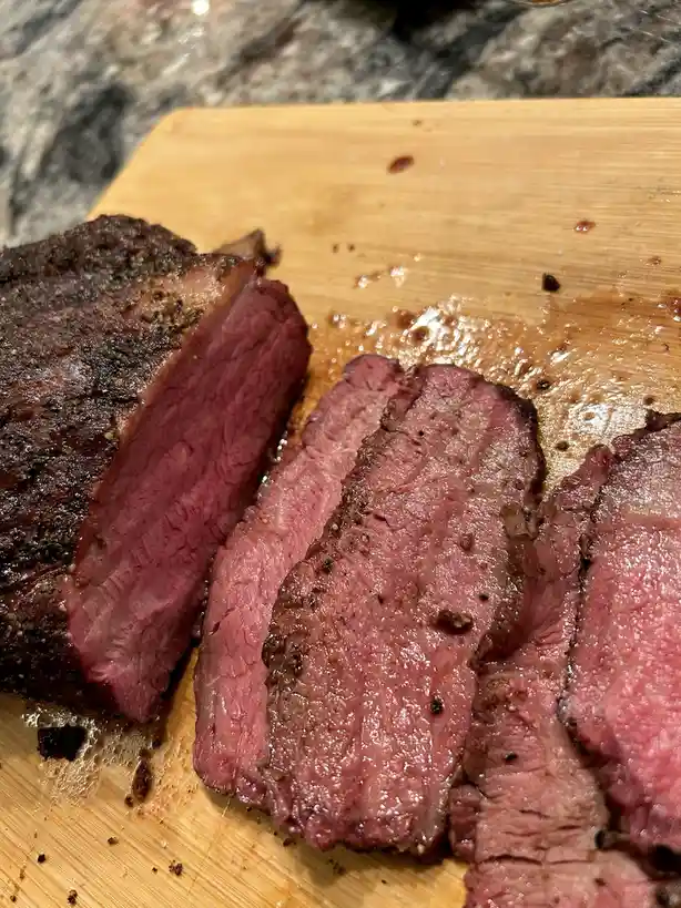 A close-up photo shows a juicy, medium-rare steak sliced on a wooden cutting board, revealing a pink interior and seasoned…