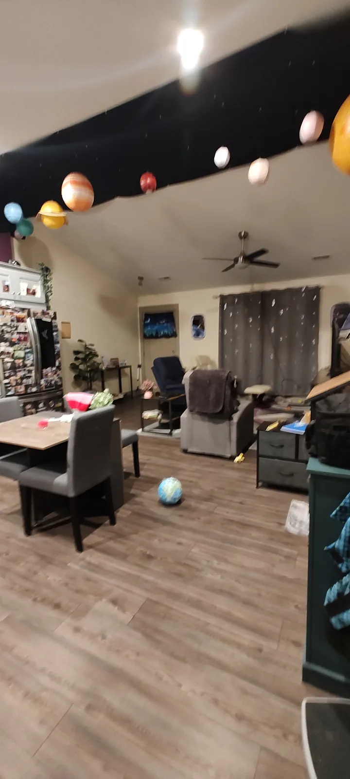 A living room with a black fabric ceiling decorated with paper cutouts of planets and stars, a globe sits on the wooden…