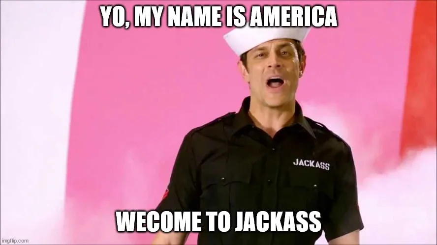 A man in a black 'JACKASS' shirt and white sailor hat stands against a pink and white background with smoke effects, mouth…