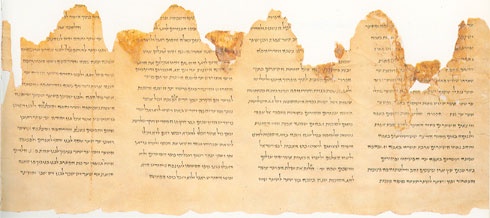An ancient, yellowed scroll with Hebrew text is visibly torn along its top edge, leaving ragged, uneven fragments. The text…