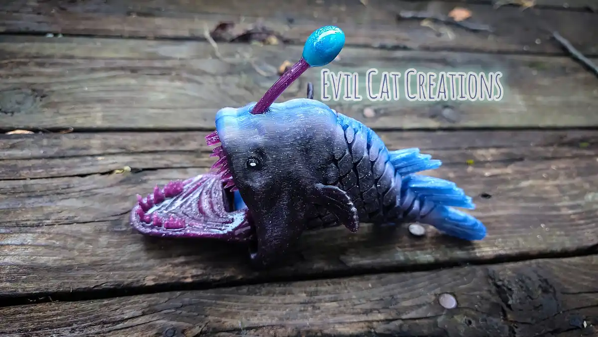 A 3D-printed, stylized anglerfish figurine with a purple and blue gradient body, sharp teeth, and a glowing blue lure on a…