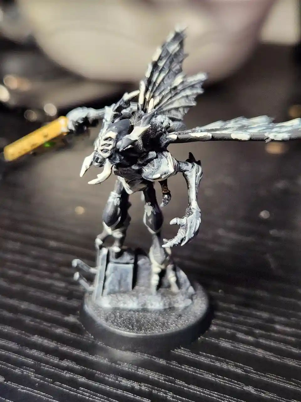 A close-up photo of a black-and-white painted miniature figurine of a demonic creature with bat-like wings, sharp teeth, and…