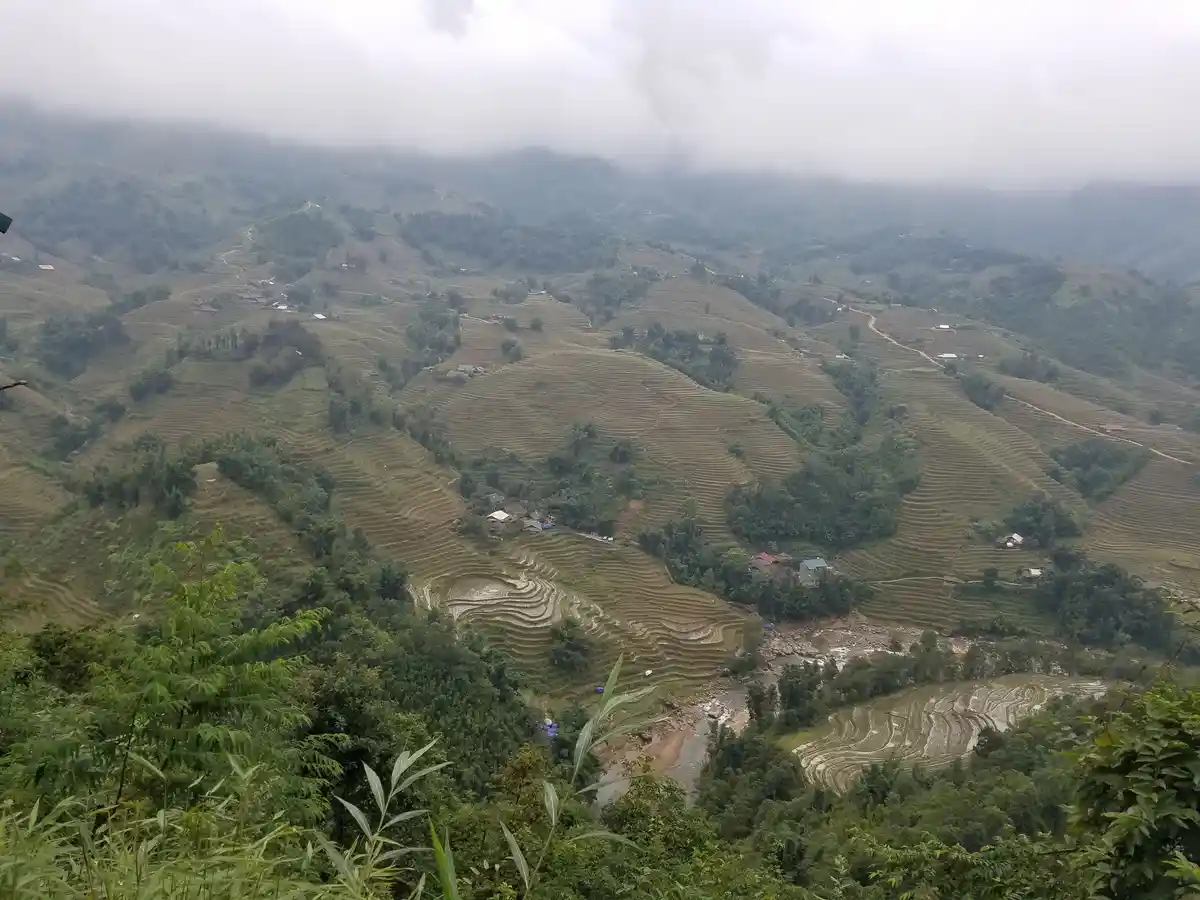 A wide-angle photograph shows expansive, mist-covered mountainous terrain with terraced rice paddies winding across the…