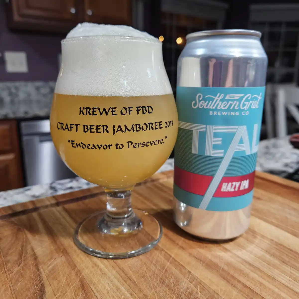 A beer glass filled with golden beer and a thick white head sits next to a can of Southern Grist Brewing Co. 'Teal' Hazy IPA…