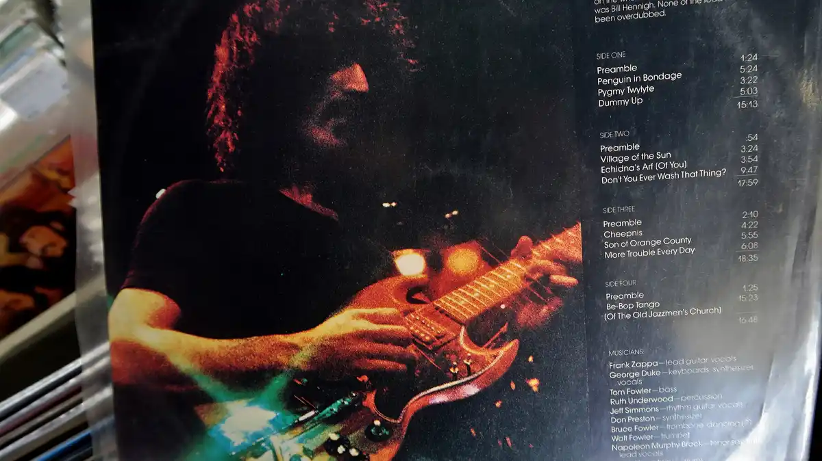 A close-up of a vinyl record sleeve showing Frank Zappa playing guitar, with the album tracklist visible on the right. The…