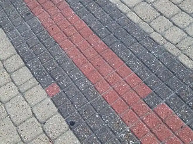 A close-up photo of a paved sidewalk with a diagonal pattern of red and gray bricks, showing a single red brick missing from…