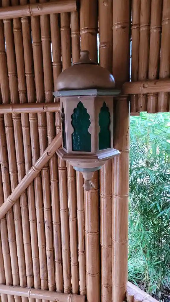 A close-up photo shows a decorative, beige-colored lantern with green glass panels mounted on a bamboo structure. The…