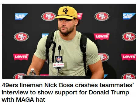 A man wearing a yellow 'MAGA' hat and a light green t-shirt sits at a press conference table with microphones, looking…