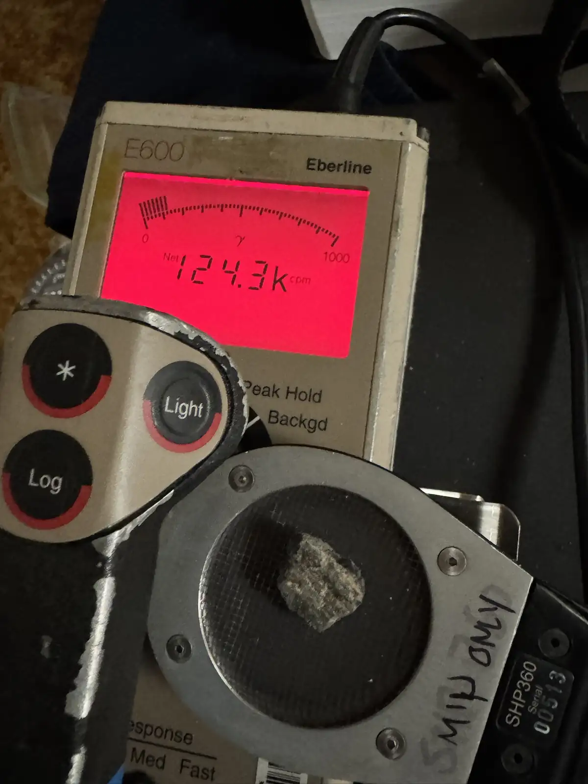 A close-up of a radioactive survey meter, model E600 by Eberline, displaying a high reading of 124.3k cpm. A small, rough…