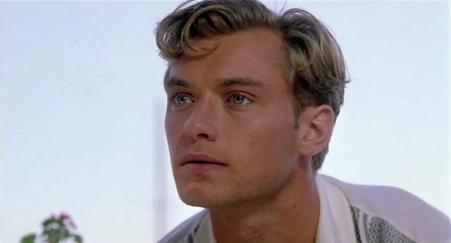 a close-up of a man with blond hair and blue eyes looking off to the side with a serious, slightly confused expression. He…