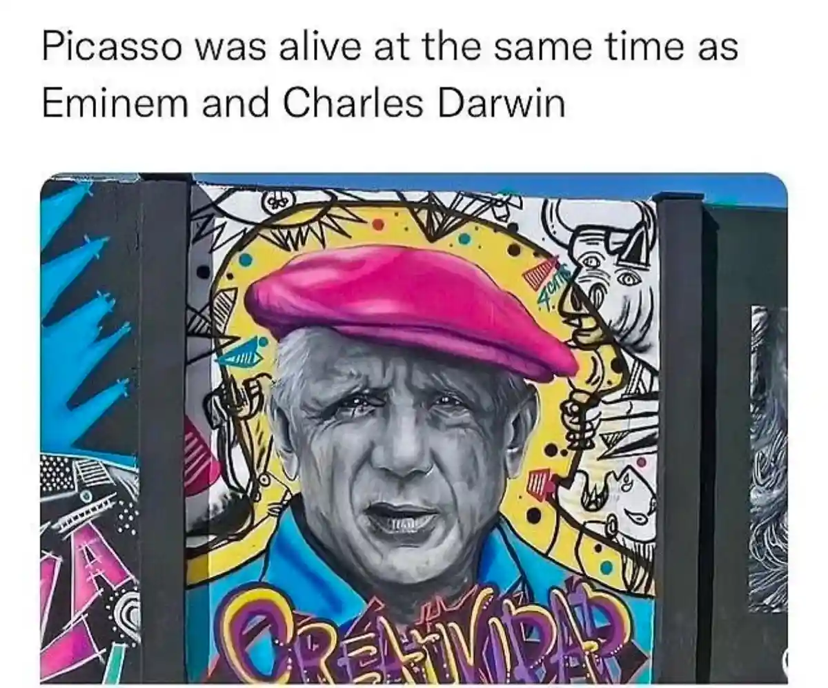 A colorful mural depicts a realistic portrait of Pablo Picasso wearing a pink beret and blue shirt, surrounded by abstract…