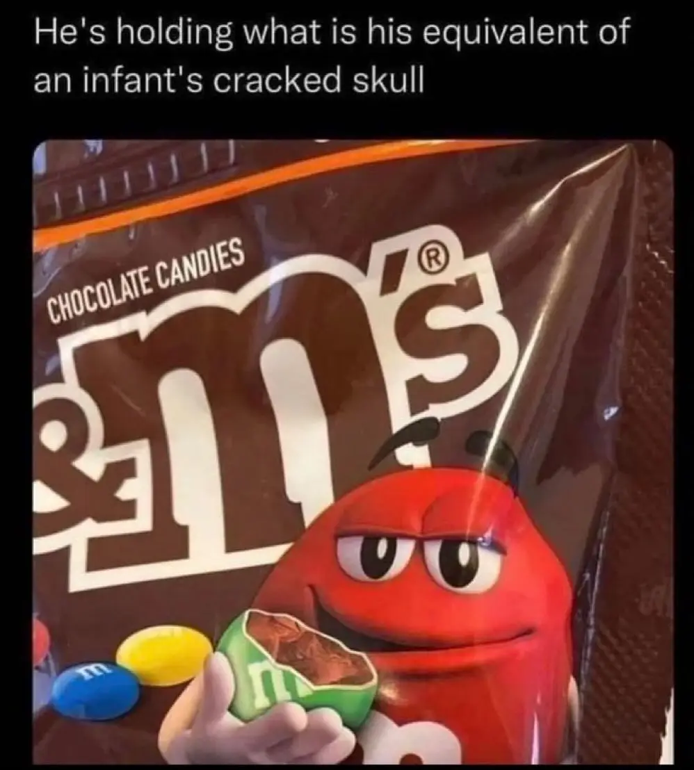 A close-up of a red M&M's character holding a green M&M candy that has been broken open, revealing the chocolate inside. The…