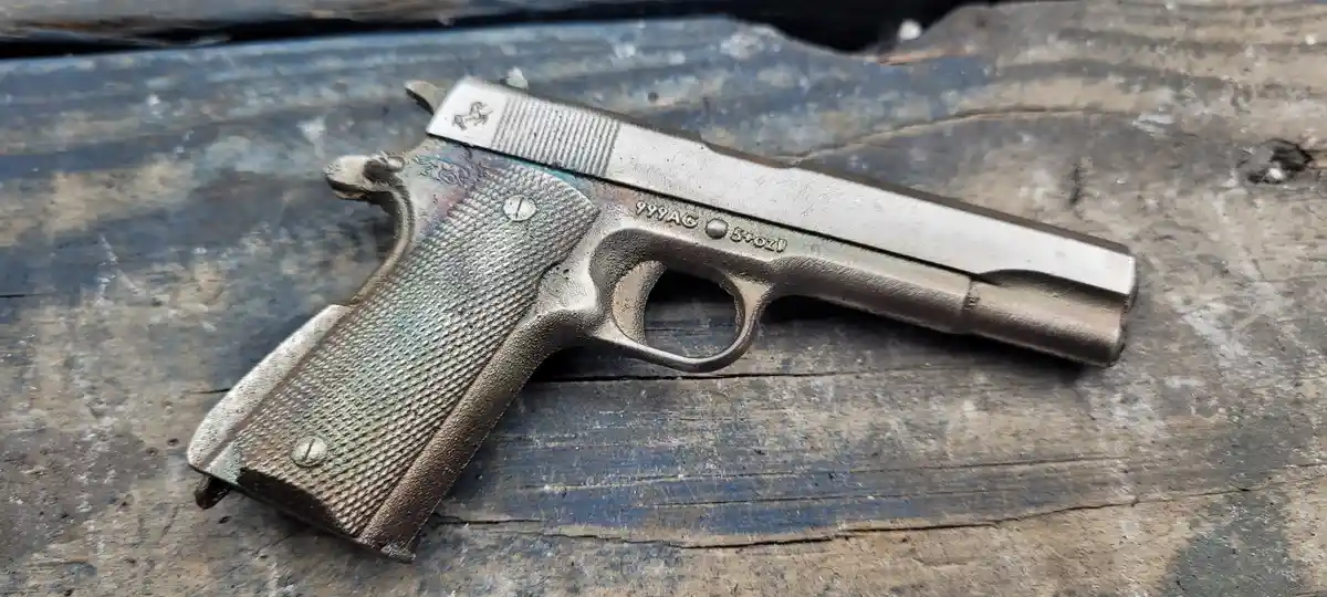 A silver-colored, textured handgun rests on a weathered wooden surface with visible grain and blue paint. The gun's slide…