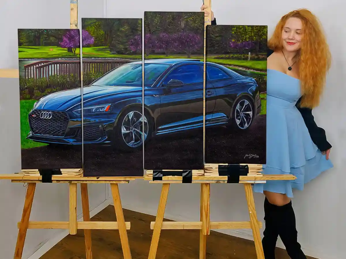A woman with long red hair stands beside four vertical canvases mounted on easels, each displaying a section of a detailed…