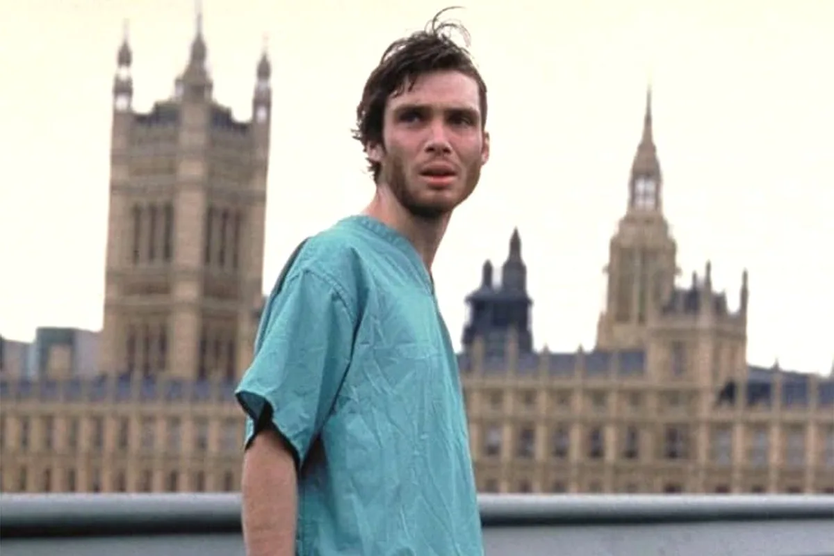 A man in a teal shirt stands on a bridge with the Palace of Westminster in the background, looking over his shoulder with a…