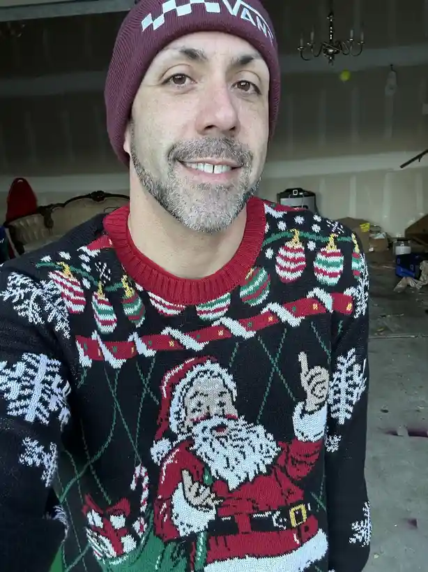 A man wearing a maroon beanie with a white checkered pattern and the word 'VANS' on it, smiles at the camera while wearing a…