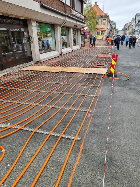a street in tromsø, norway, is covered with orange heating pipes laid out in a grid pattern on asphalt, secured by metal…