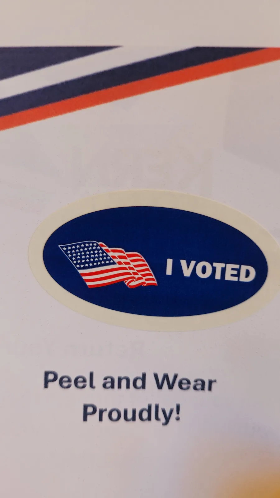 A close-up photo shows a standard U.S. 'I VOTED' sticker with an American flag graphic, attached to a paper that reads 'Peel…