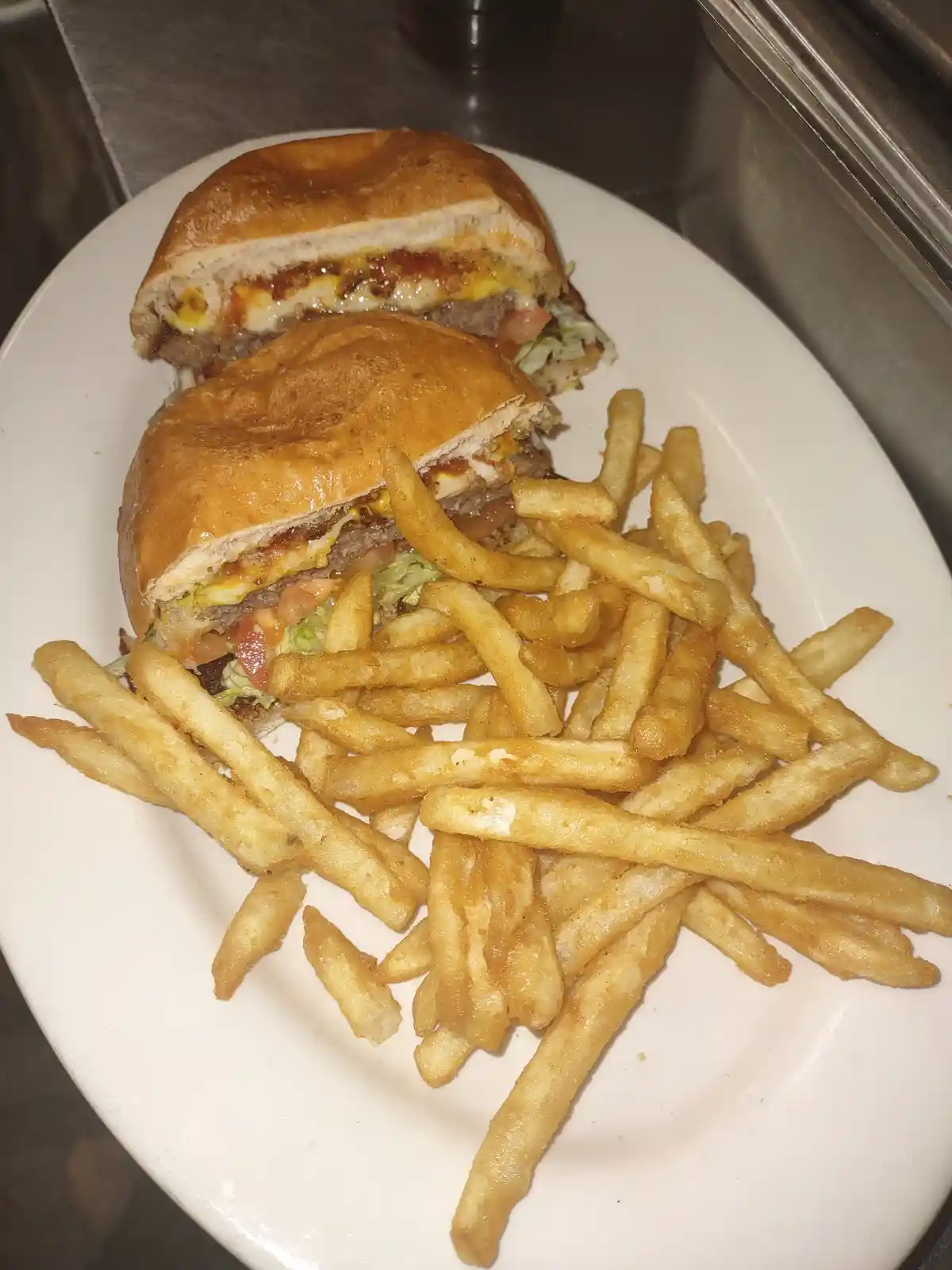 A plate of a large burger cut in half, revealing melted cheese, tomato, lettuce, and meat patty, served with a generous pile…