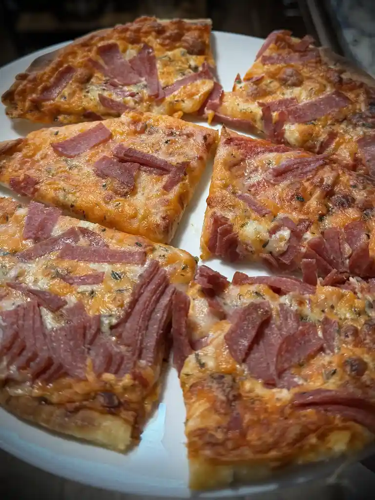A close-up photo shows a pizza cut into slices on a white plate, generously topped with melted cheese and numerous slices of…