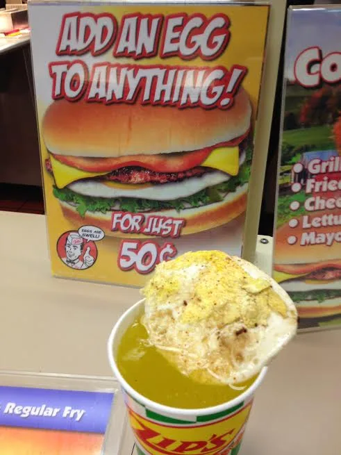 A close-up photo shows a cup of golden-brown french fries topped with a fried egg, sitting on a counter. Behind it, a bright…