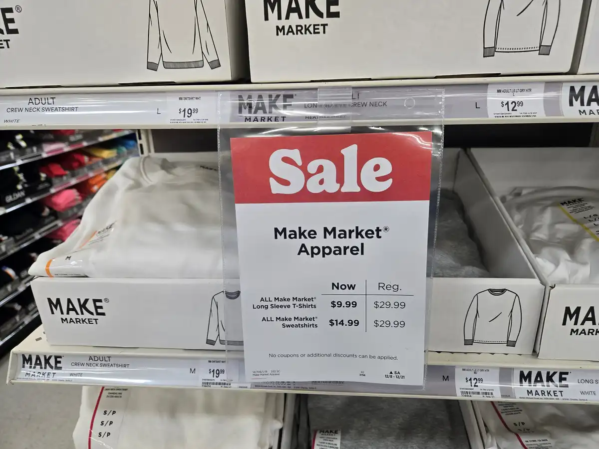 A store shelf displays boxes of 'Make Market' brand apparel, including long sleeve t-shirts and sweatshirts, with a…