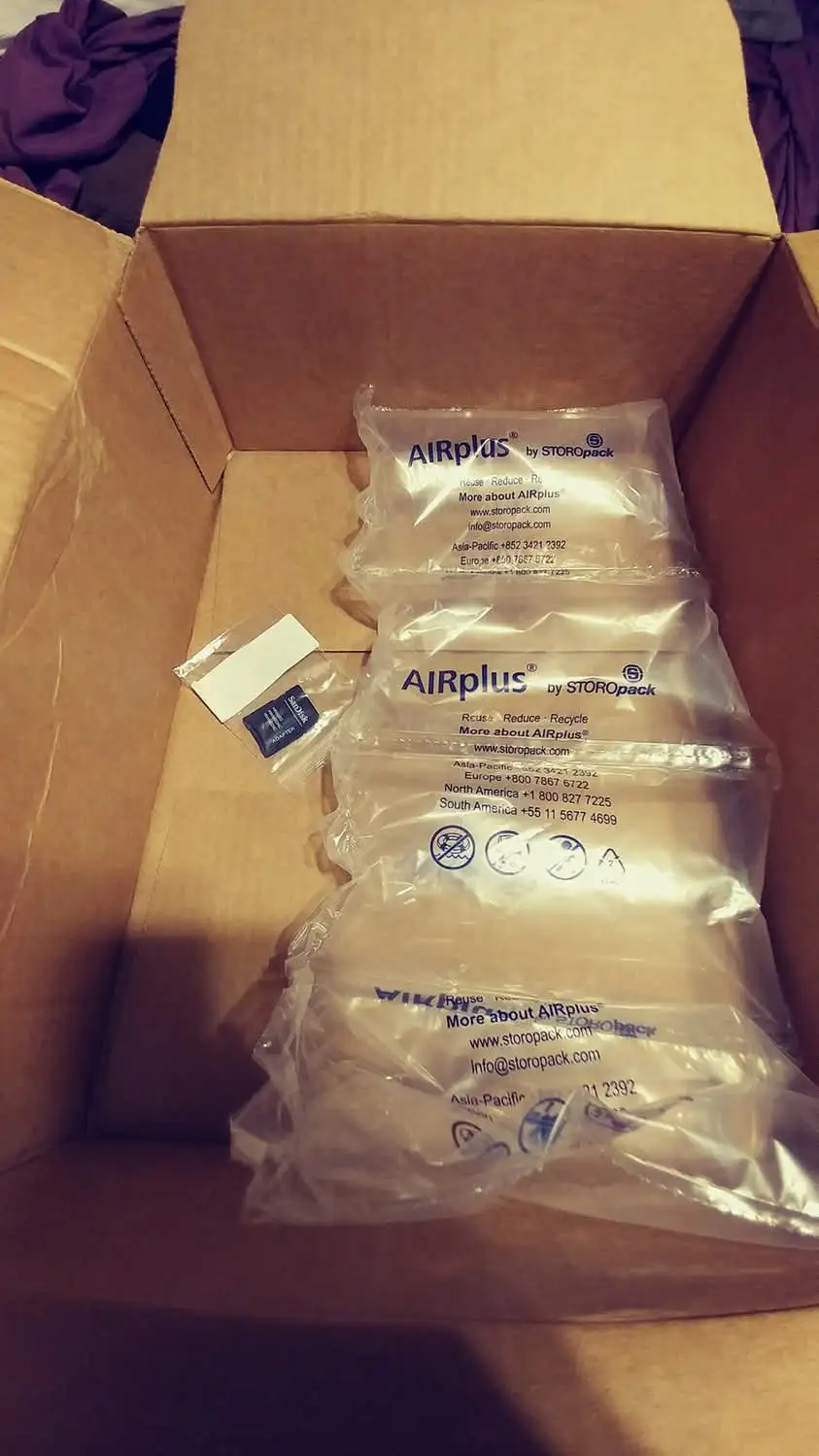 A cardboard box contains multiple clear plastic air pillows branded 'AIRplus by STOROpack' with contact info and recycling…