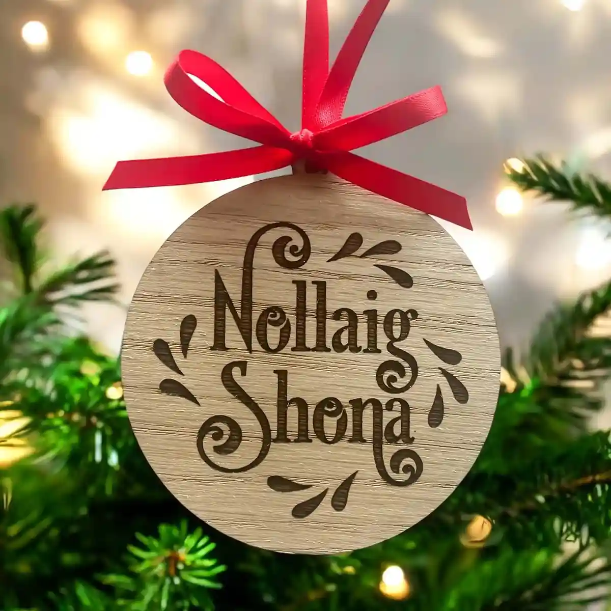 A close-up of a round wooden Christmas ornament hanging from a red ribbon against a blurred background of green pine…
