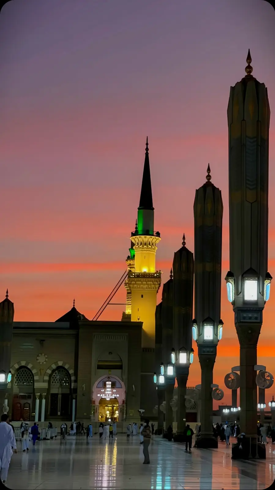 A photograph of a grand mosque at sunset, featuring illuminated minarets and ornate architecture against a vibrant orange…