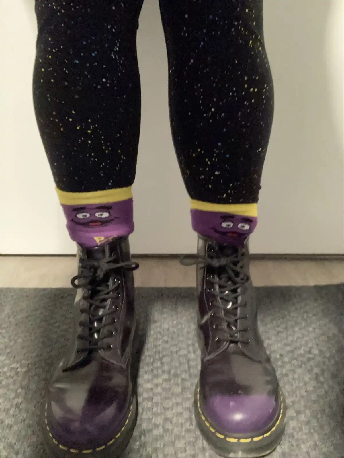 A close-up shot of a person's legs wearing black leggings with colorful speckles, paired with purple socks featuring a…