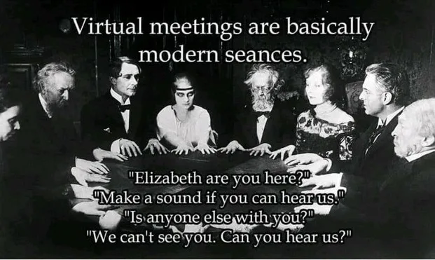 A black-and-white photo of seven people gathered around a table, hands placed on its surface as if conducting a séance…