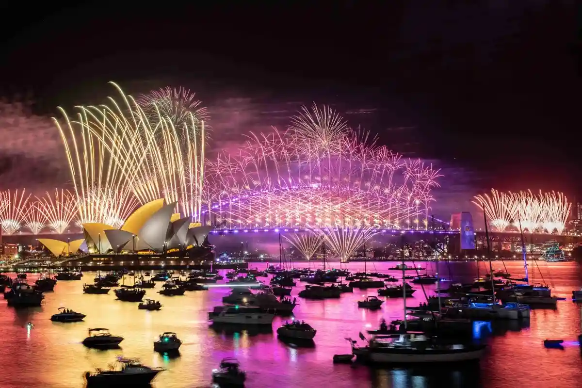 A vibrant nighttime photograph of Sydney Harbour, featuring the iconic Sydney Opera House and Harbour Bridge illuminated by…