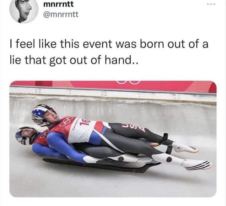 Two athletes in USA luge uniforms lie prone on a sled, appearing to be asleep or exhausted, as they glide down an icy track…