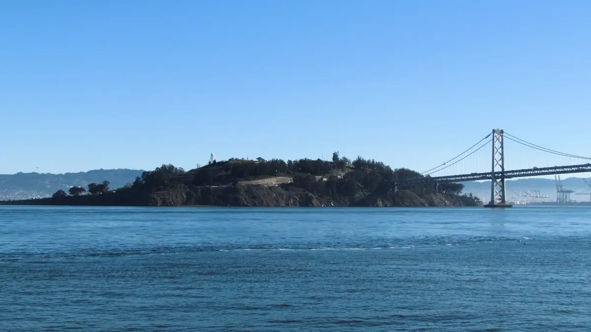 A scenic view of the San Francisco Bay featuring the Bay Bridge and Alcatraz Island under a clear blue sky. The overlaid…