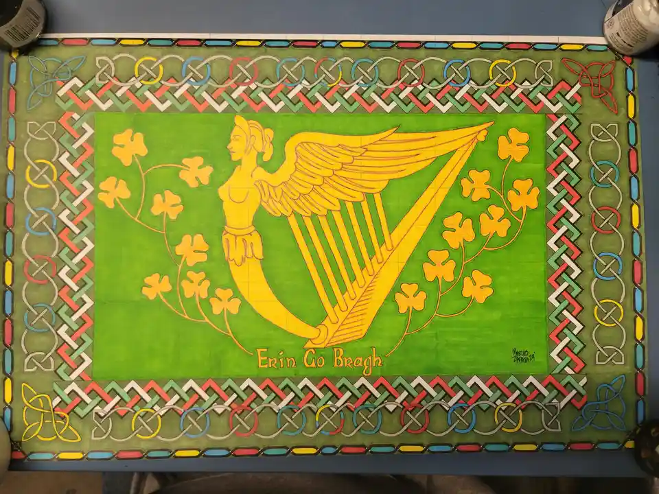A hand-drawn, colorful artwork on green paper features a golden harp with wings and a human upper body, surrounded by…