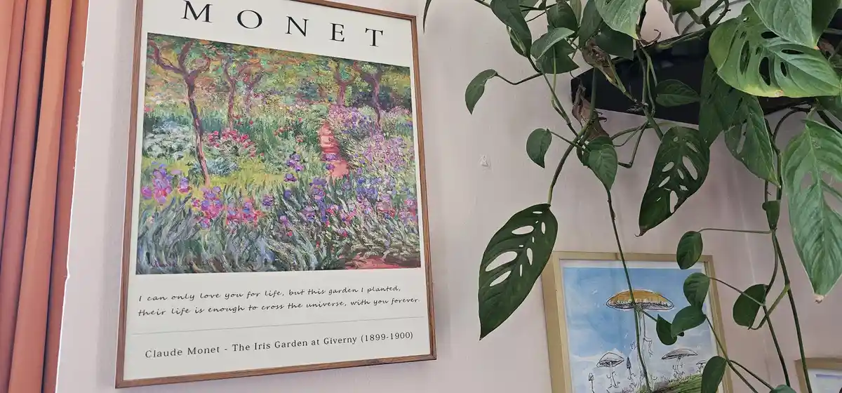 A framed print of Claude Monet's 'The Iris Garden at Giverny' (1899-1900) hangs on a wall next to a large, leafy monstera…