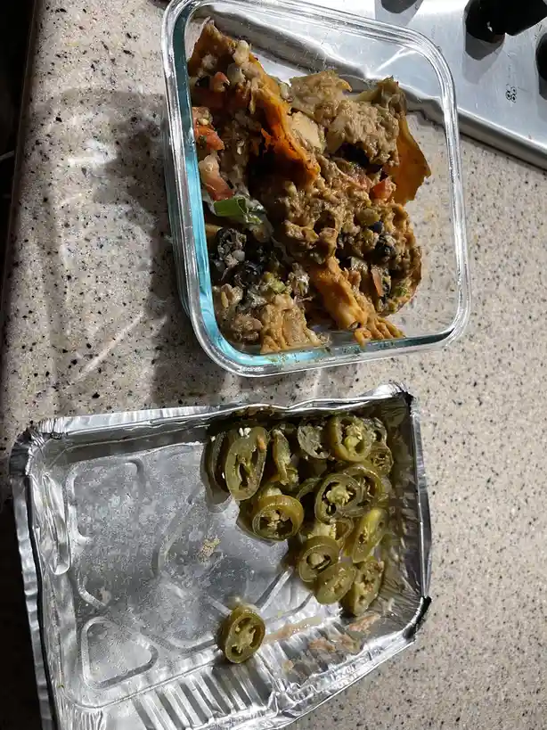 A photo shows a nearly empty glass food container with leftover nachos and a foil tray with only a few jalapeño slices…