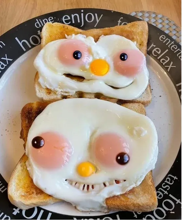 Two sunny-side-up fried eggs are placed on separate slices of toast, arranged on a plate with words like 'dine', 'enjoy'…