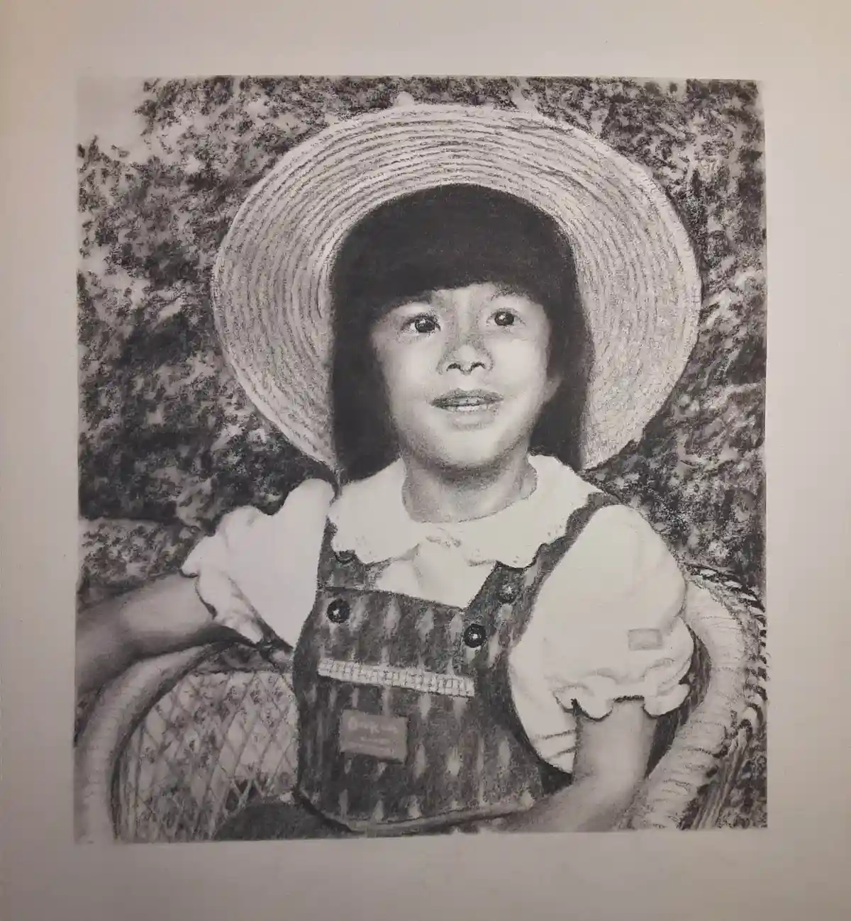 A black-and-white pencil drawing of a young child wearing a large, wide-brimmed straw hat and overalls over a collared…